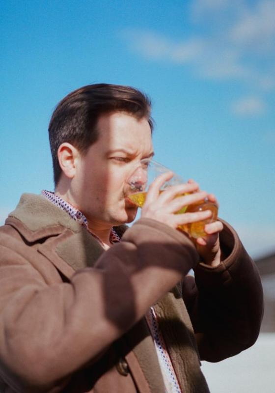 Andy drinking a pint intently outside against a blue sky.