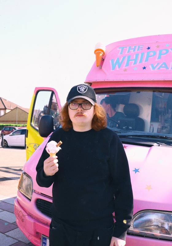 Jack stands in front of a pink van holding an ice cream cone. 