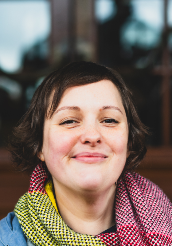 Josie Long looking straight at the camera in front of reflective door window and smiling