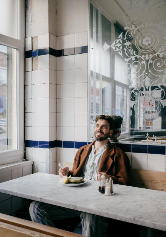 Joz sitting in a white, airy cafe with a mirror behind him
