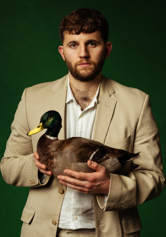 Rory stands in a beige suit, holding a live duck.