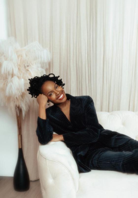 Sharon reclines on a white cushioned sofa holding with a big smile.