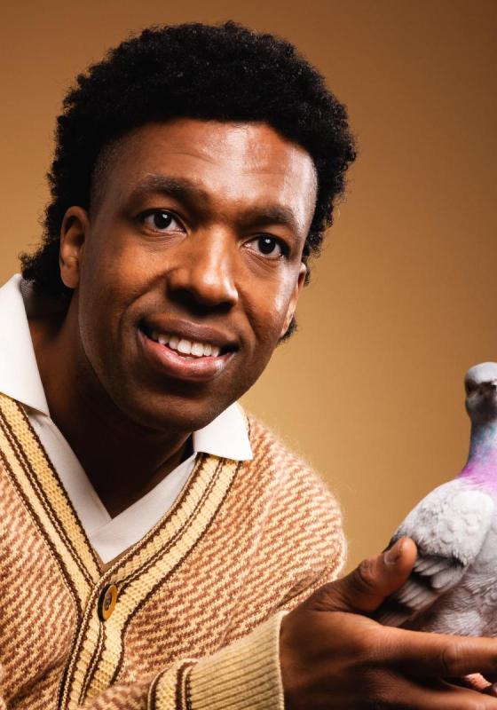 Toussaint looks towards the camera carefully holding a pigeon in his cupped hands.