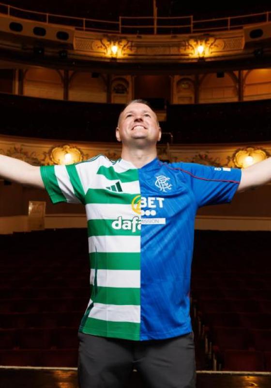 A person in a football jersey (one half of which is blue and the other white and green stripes) stands on a stage with the auditorium behind them, arms open wide. 