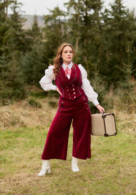 Woman standing in a field in a red pantsuit, holding a briefcase