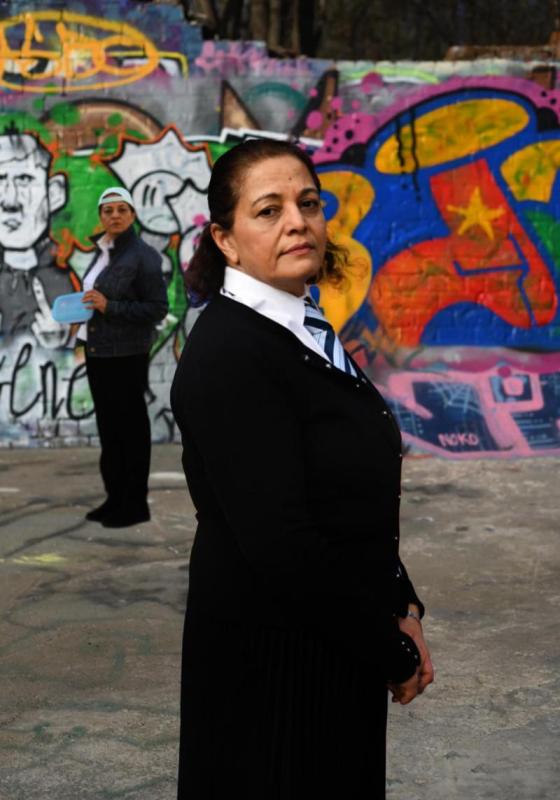 The actor standing in front of a graffiti wall in school uniform. The other character stands apart in the back.