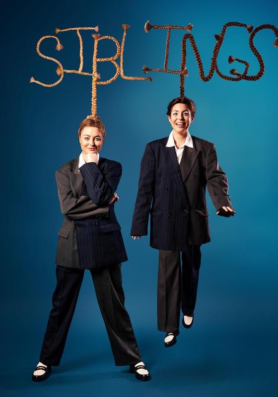 Siblings wearing oversized suits with their hair sculpted to spell out 'Siblings'