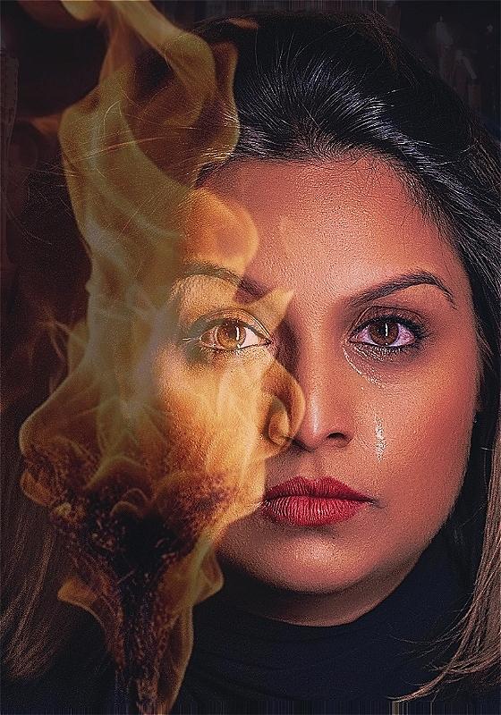 #A close up of a woman's face. On one side, a fire blares across her face using the magic of editing. On the other, a single tear.