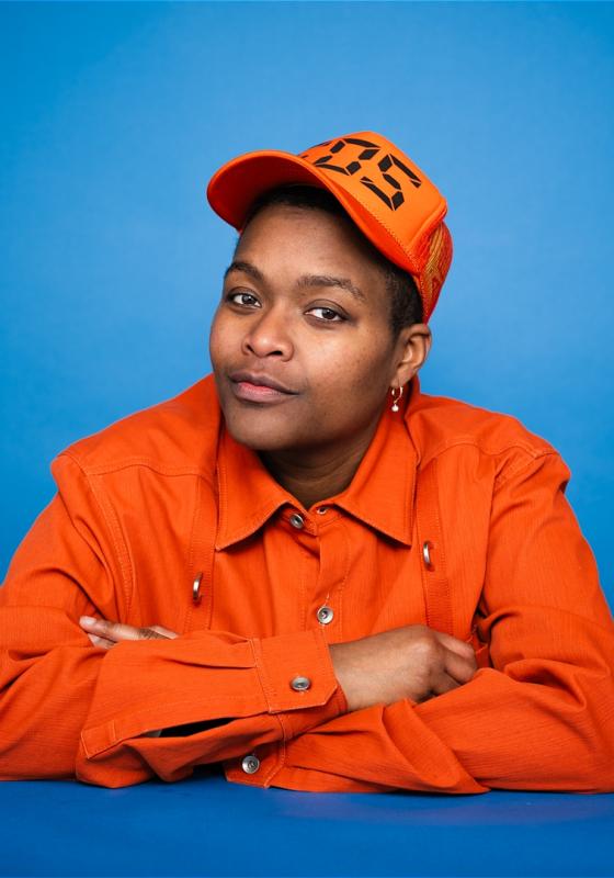 Sam jay in orange outfit against blue background