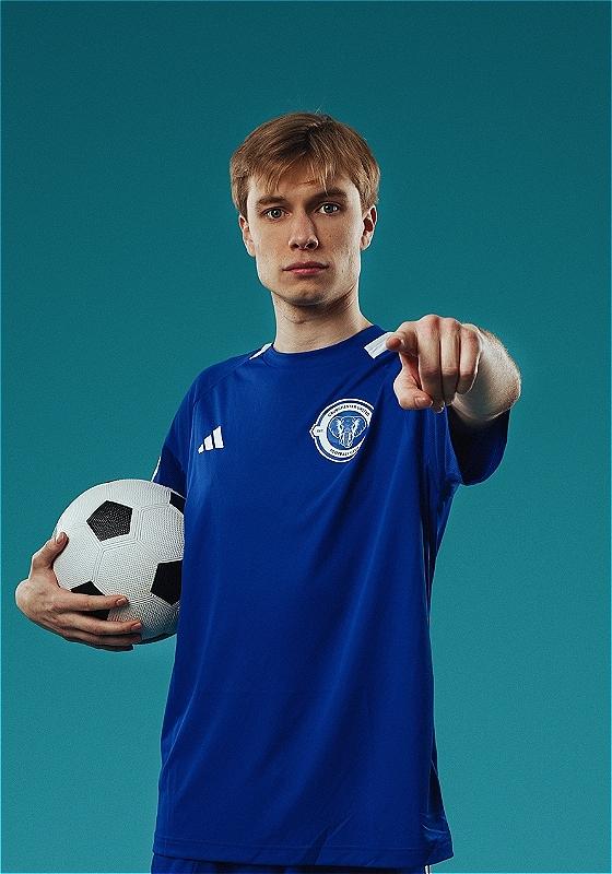 Ted points at the camera, holding a football in his other hand and wearing the royal blue jersey of Crudchester United