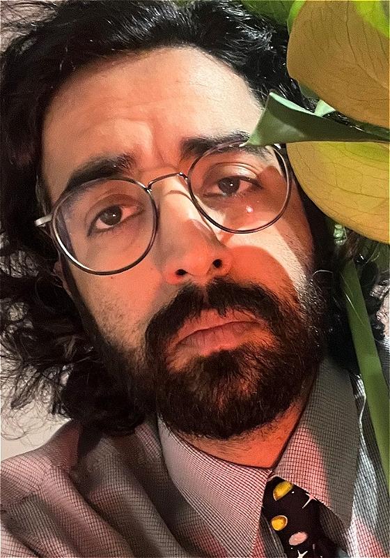 A bespectacled man sulks next to a plant