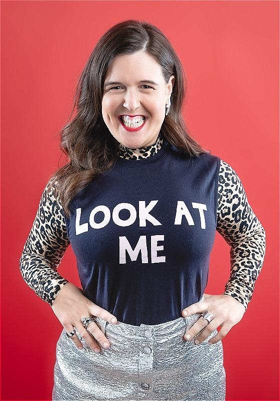 Rosie Jones stares at the camera with a brilliant smile and a top that says 'LOOK AT ME' in bold white letters