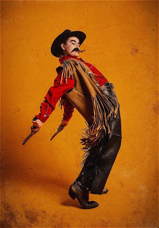 A mustachioed cowboy thrusts their pelvis forward and their gun-wielding hands fly back from the momentum. A cigar hangs from their mouth and tassels hang from their jacket. 