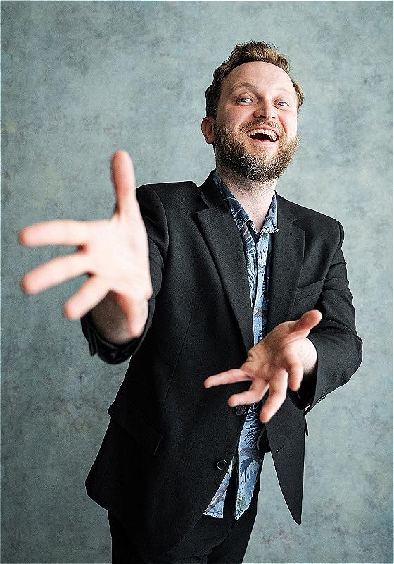 Crowley outstretches his hand to the camera in a fascinating manner while wearing a blazer