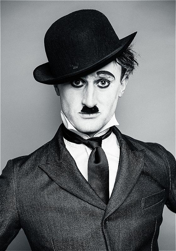 A black and white close up photograph of a performer dressed and styled as Charlie Chaplin.