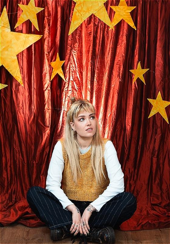 Performer sits in front of a red cloth background with stars cut out.