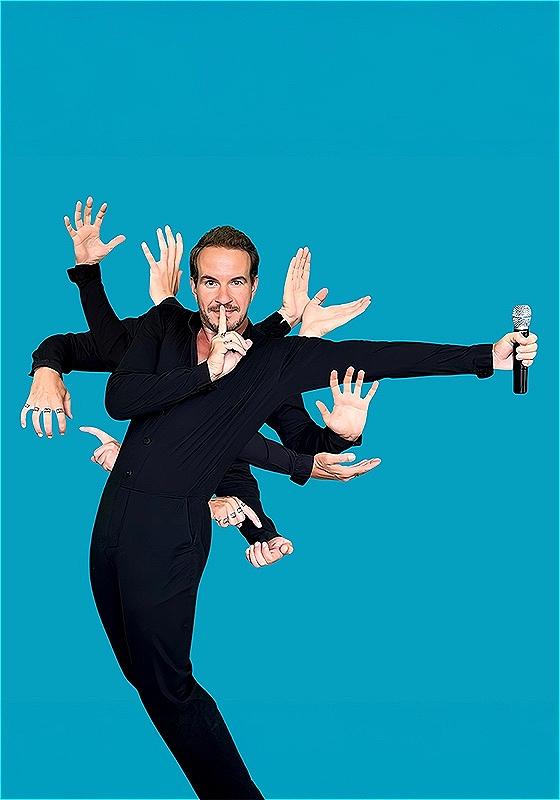 A man dressed in black holds his finger to his lips in a shushing manner whilst eleven hands sprout from his body in an assortment of different positions. The hand stretched furthest from the man holds a microphone.