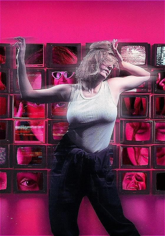 A woman dances chaotically in front of a 6x6 wall of TV screens, depicting another woman's face in a variety of positions against a hot pink backdrop.