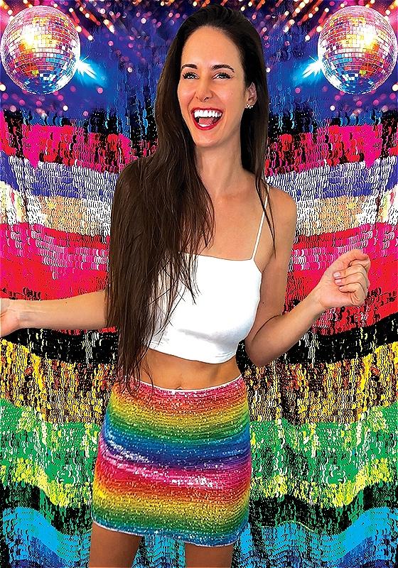 Brooke stands in front of an extremely glittered backdrop filled with colour, disco balls, patriotic red and blue, and the numbers '2' and '2' which are stacked on top of each other in the bottom left corner.