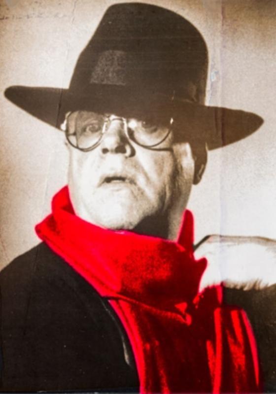Black and white photo of Truman Capote wearing a hat and bright red scarf.