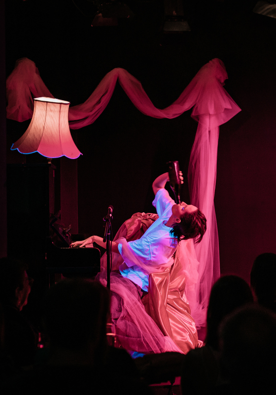 A performer drinks a bottle whilst playing a piano.