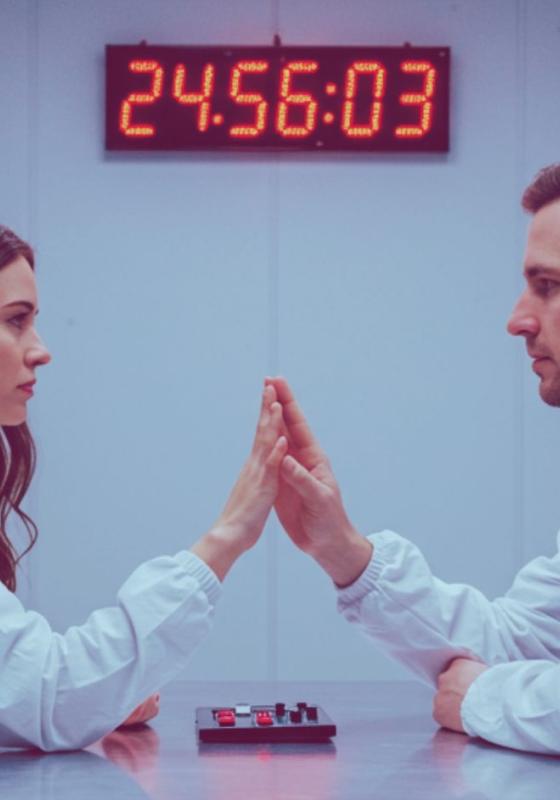 Two people dressed in white touch hands gently over a table. 