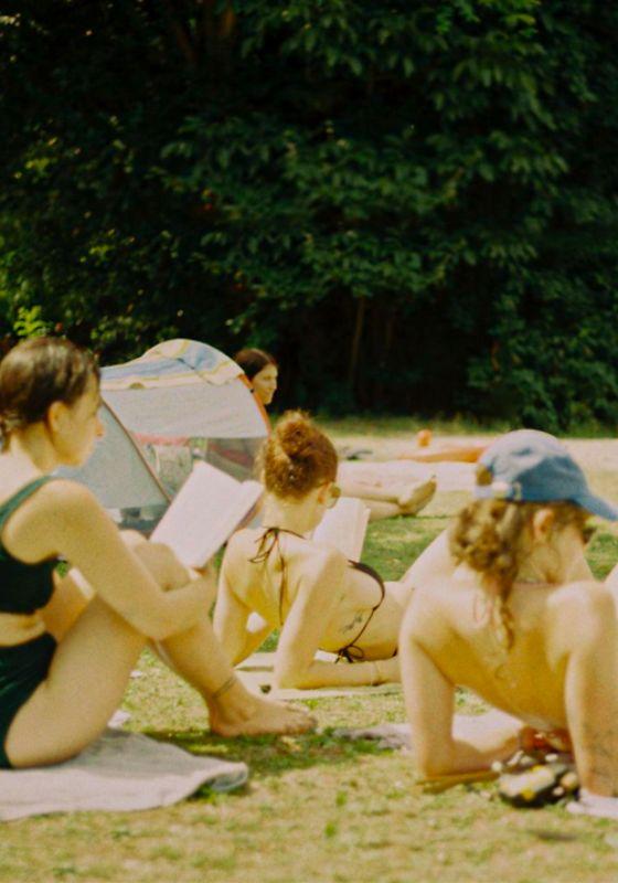 A grainy film shot of women sunbathing in a garden, some are reading.