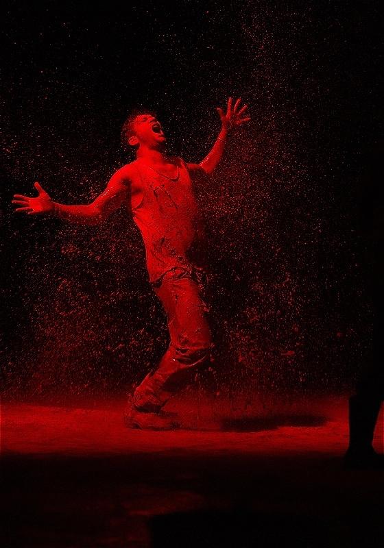 A performer covered in red dust cries out in anguish.