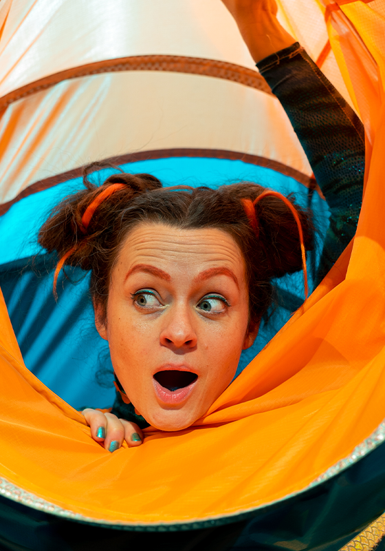 A woman smiles peering out of a large orange and blue nylon tube