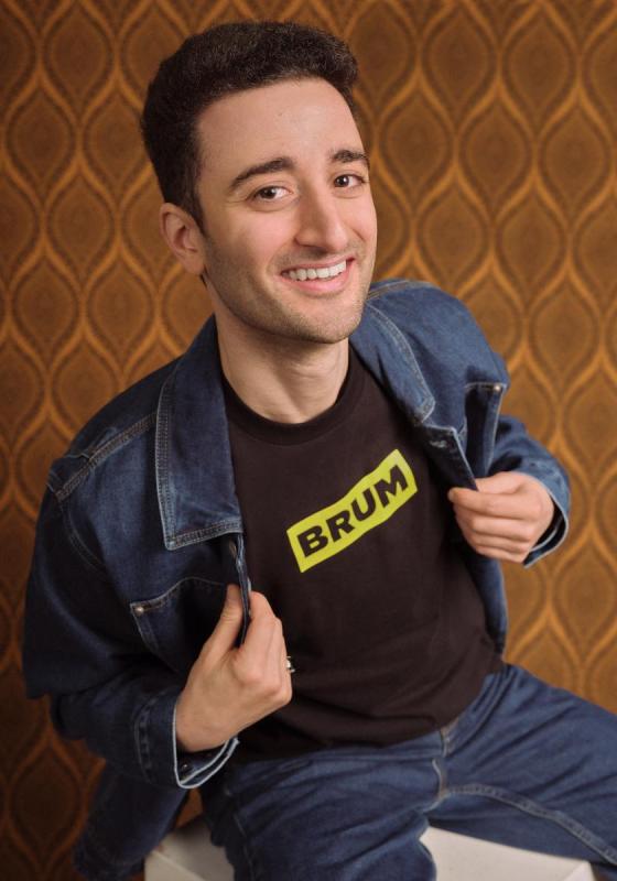 Hasan grinning whilst exposing his t-shirt with the word BRUM written on it.