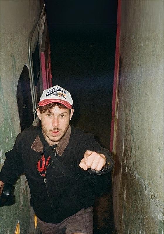 The image depicts someone walking through a narrow tunnel pointing to the camera.