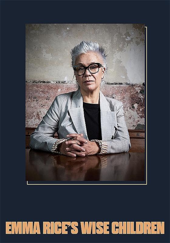Emma Rice sat at a wooden table in front of a rustic looking wall, with text below reading "Emma Rice's Wise Children"