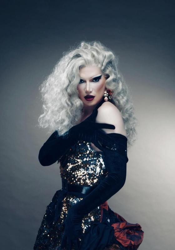The performer in a grey wig and wearing a ballgown with black opera gloves