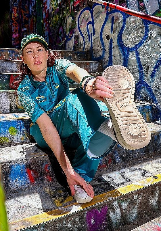 Woman standing sideways on a wall with graffiti.