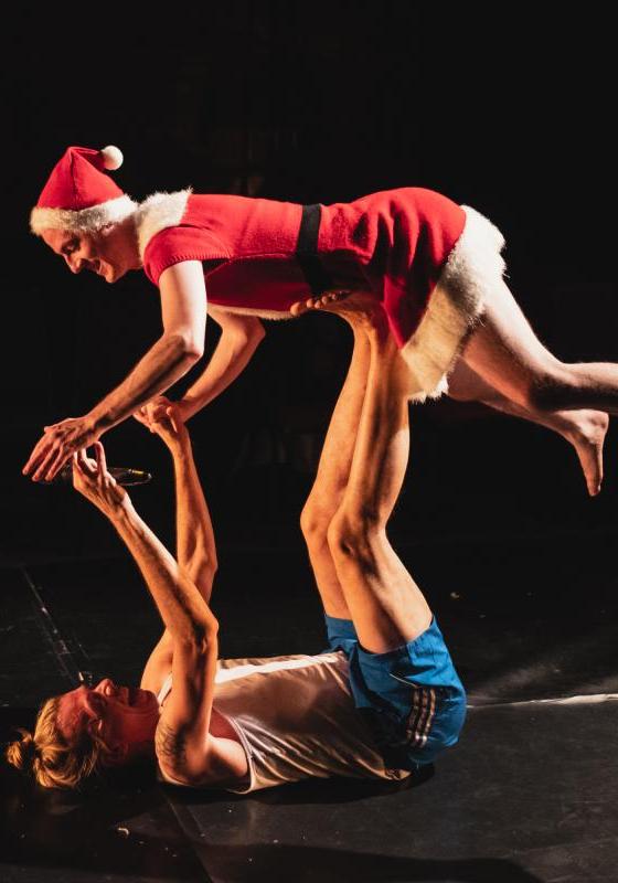 Two performers holding a balancing lift pose, one wears a red and white santa costume.