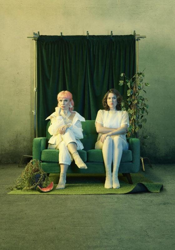 The performers sitting awkwardly on a green sofa dressed in white. The photo has a green, haunting tint.
