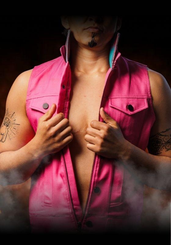 A performer wears a pink leather waistcoat over a bare chest as steam rises.