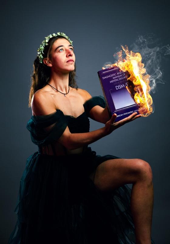 Performer kneels in a black dress and holds a burning book.