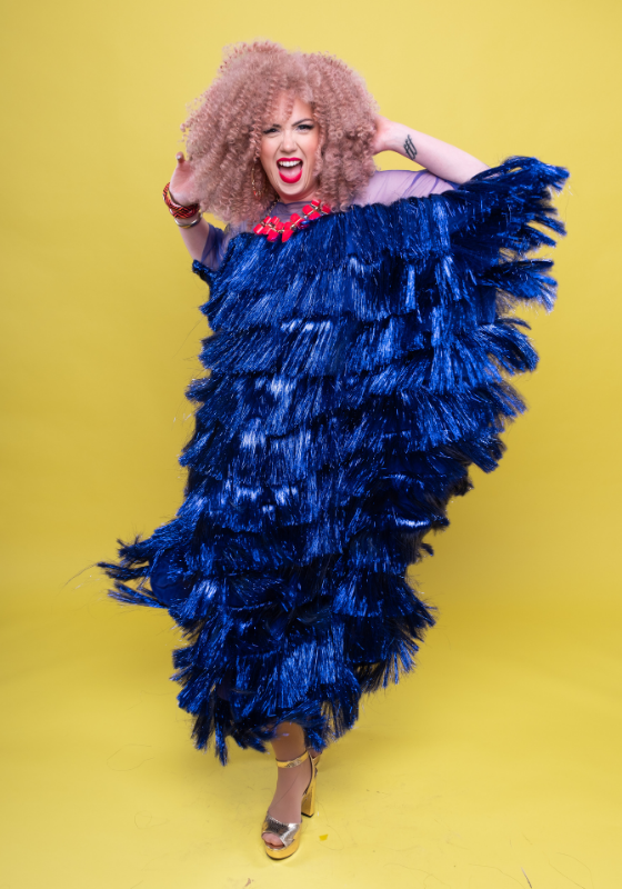 Frisky wearing a statement red necklace and a large dark blue flapper dress.