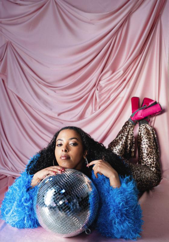 The performer rests her head on a large disco ball against a satin pink backdrop.