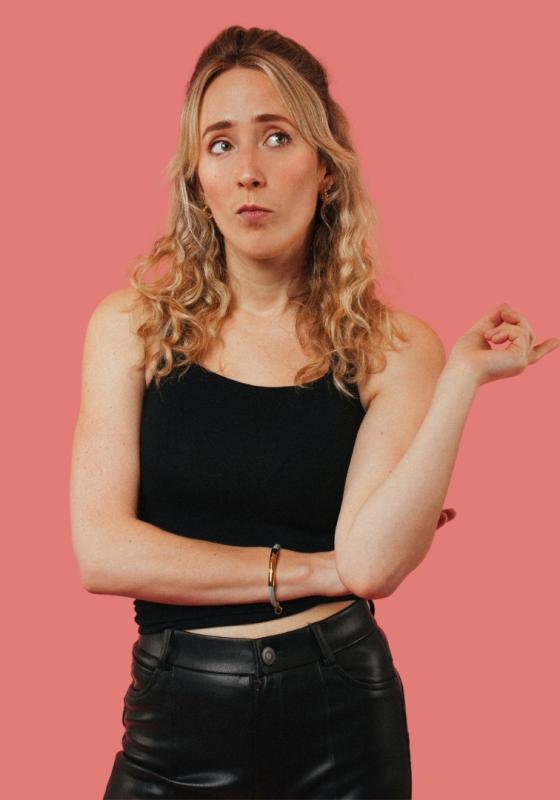 Kate-Lois wearing all black looking sassy while glancing off camera. Pink background.