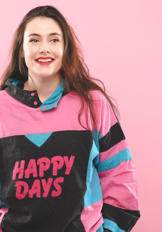 Marjolein in front of a pink background wearing a top that says happy days