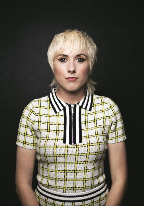 Headshot of Maisie Adam looking directly into the camera wearing a patterned, collared, short sleeve top.