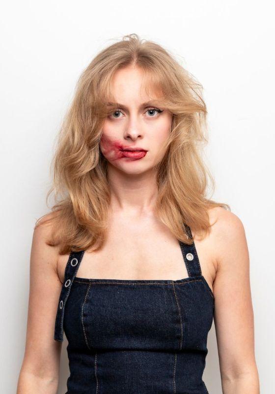 Olivia facing the camera straight faced with red lipstick smudged across their face