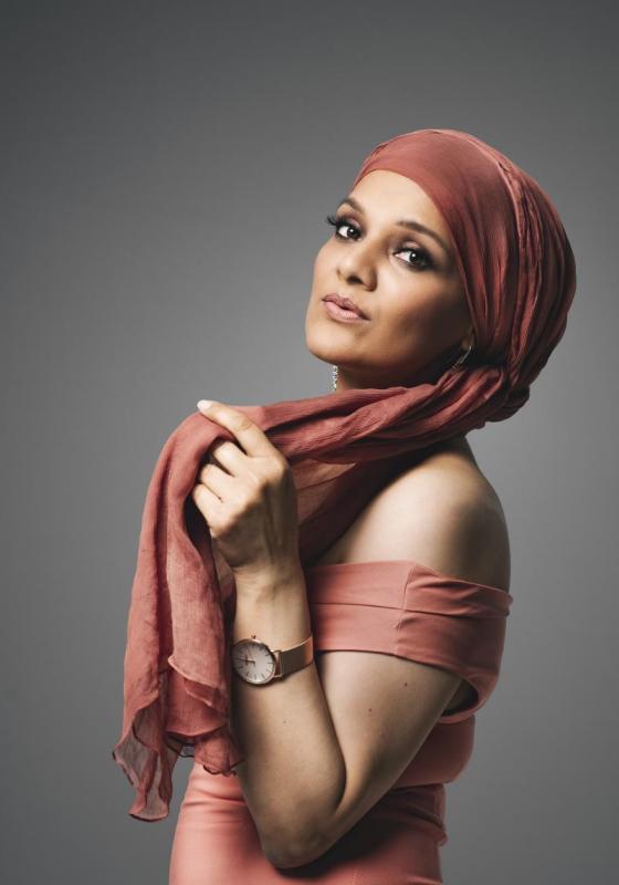 Sadia wearing a pale orange headscarf and dress against a grey background.