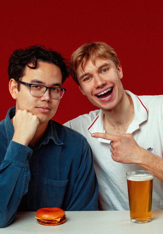 James and Ted sit next to each other jovially with a burger and a pint.