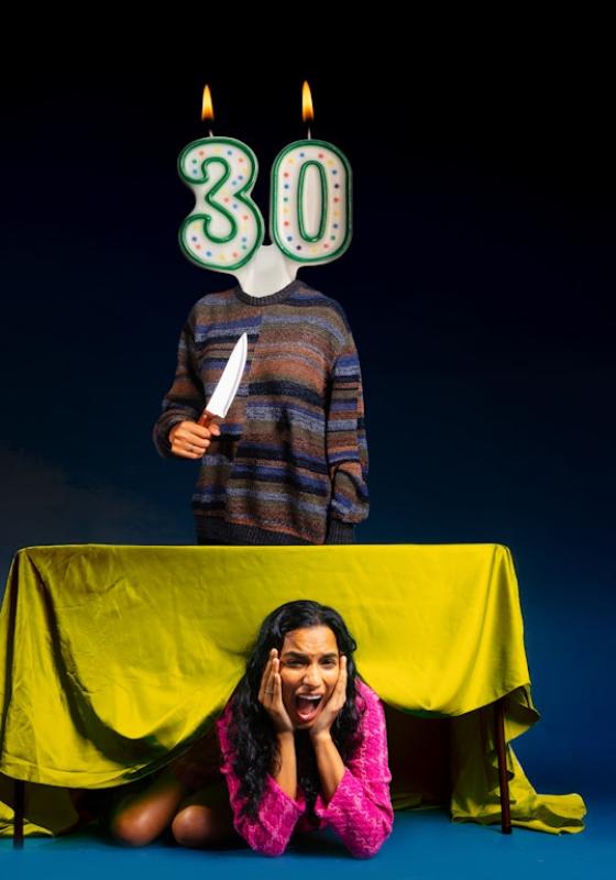 Abby hiding under a table while a person with a 30th birthday candle face looms above