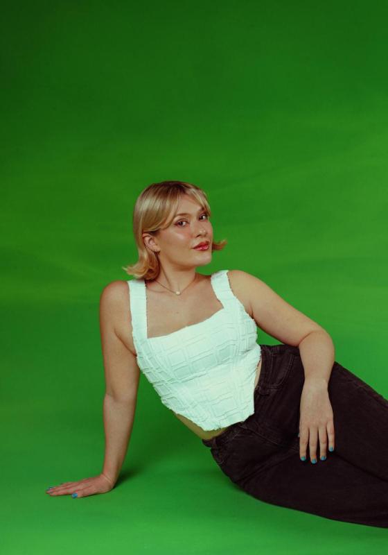 Cecily posing in a white corset style top with a dark green background.