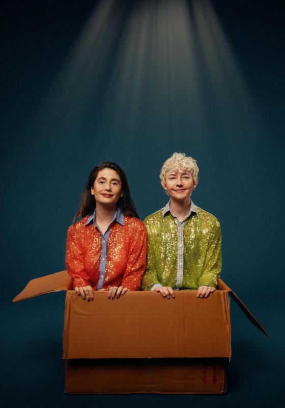 The duo Britney wearing sparkly jackets are sat in a cardboard box under a spotlight.