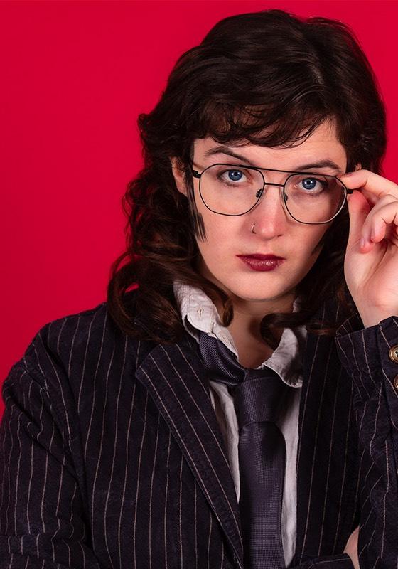 A photo Roger wearing a pinstripe suit and loose tie with sideburns and glasses.